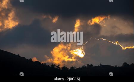 Tramonto con cielo nuvoloso e sole nascosto dietro nuvole Foto Stock