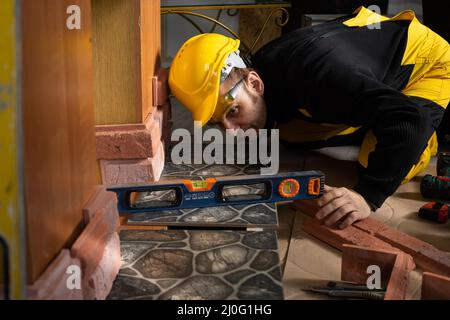 Un operaio di costruzione controlla con una livella di spirito che le mattonelle di terracotta sono disposte uniformemente in tutte le zone. Vestito in p. Personale Foto Stock