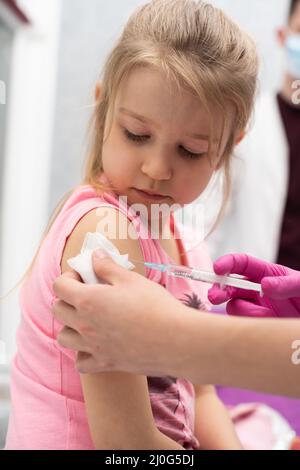 Il medico sta somministrando un'iniezione ad una bambina. Il bambino si trova in una ciotola soffocante. Vaccino preventivo per bambini piccoli. Clos Foto Stock