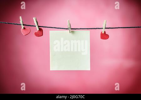 Carte di carta bianca appese su abiti con mini clip wiyh insieme a forme rosse del cuore Foto Stock