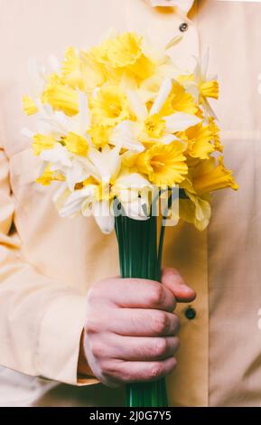 Un uomo in una camicia gialla che tiene un bouquet di fiori di naffodils Foto Stock