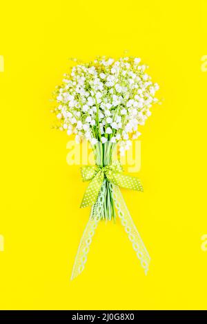 Bouquet di giglio della valle fiori con un arco e nastro su sfondo giallo vista dall'alto da vicino Foto Stock