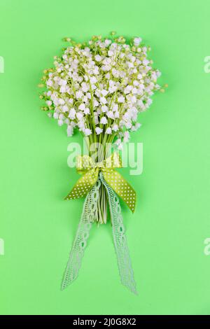 Bouquet di giglio della valle fiori con un arco e nastro su sfondo verde vista dall'alto da vicino Foto Stock