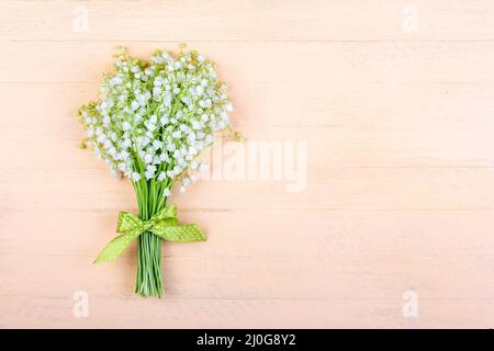 Bouquet di giglio della valle fiori con un arco verde su sfondo rosa di legno con uno spazio copia Foto Stock