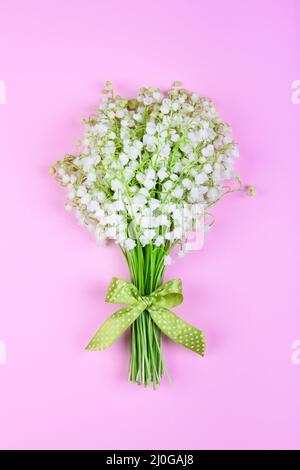 Bouquet di giglio della valle fiori con un arco verde su uno sfondo rosa primo piano Foto Stock
