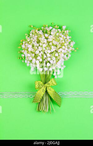 Bouquet di giglio della valle fiori con un arco verde e nastro su sfondo verde vista dall'alto da vicino Foto Stock