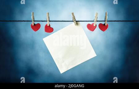 Carte di carta bianca appese sui vestiti insieme con le forme rosse del cuore Foto Stock