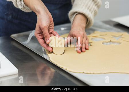 Pasticceria tagliando l'impasto a forma di cuore mentre si fanno i biscotti nella cucina della panetteria. Foto Stock