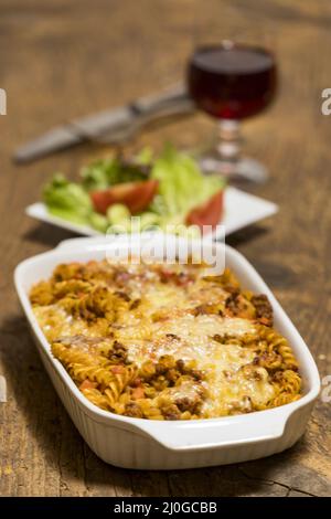 Pasta al gratin con insalata su legno Foto Stock