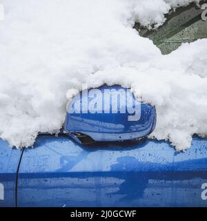 Un frammento di un'auto blu bagnata ricoperta di neve con uno specchietto retrovisore ripiegato. Foto primo piano Foto Stock