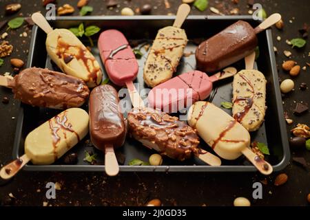 Assortimento di vari gelati a base di papsicle, cioccolato bianco e scuro, con mandorle, fondo arrugginito Foto Stock