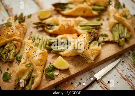 Asparagi verdi al forno avvolti in pasta sfoglia. Servita su tavola di legno. Con messa a fuoco selettiva Foto Stock