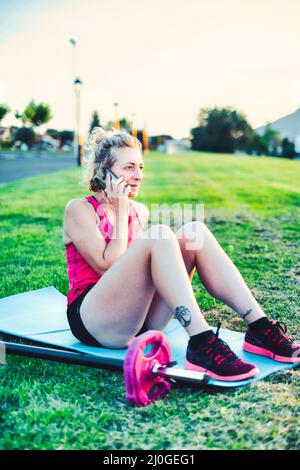 Vera giovane matura donna caucasica in un abbigliamento sportivo che parla con il suo cellulare nel parco in un pomeriggio soleggiato. Foto Stock