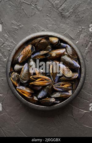 Cozze di mare fresche e grezze in ciotola nera in ceramica su sfondo di pietra scuro Foto Stock