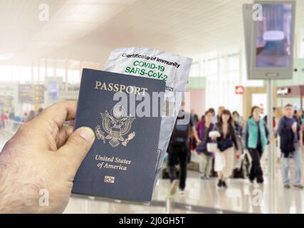 Mano che tiene un passaporto degli Stati Uniti con una carta rugosa Coronavirus Covid 19 certificato di immunità offuscato aeroporto in background Foto Stock