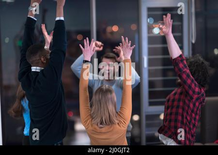 I giovani uomini d'affari multietnici che si divertono a celebrare il successo aziendale condiviso o la vittoria in carica. Sorridente multirazziale diversi dipendenti sentire Foto Stock