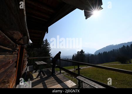 19 marzo 2022, Baviera, Großweil: Un uomo gode del sole in una storica capanna alpina sui terreni del museo all'aperto Glentleiten. Dopo la polvere del Sahara, il sole primaverile si ripresenta nel cielo nuvoloso. Foto: Angelika Warmuth//dpa Foto Stock