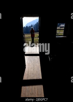 19 marzo 2022, Baviera, Großweil: Il sole getta una lunga ombra attraverso la porta di uno storico rifugio alpino sui terreni del Museo all'aperto Glentleiten. Dopo la polvere del Sahara, il sole primaverile si ripresenta nel cielo nuvoloso. Foto: Angelika Warmuth//dpa Foto Stock