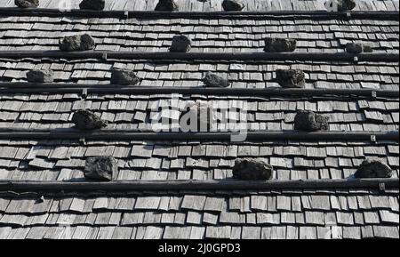 19 marzo 2022, Baviera, Großweil: Le pietre pesano le tegole di legno su un tetto sui terreni del museo all'aperto Glentleiten. Dopo la polvere del Sahara, il sole primaverile si ripresenta nel cielo nuvoloso. Foto: Angelika Warmuth//dpa Foto Stock