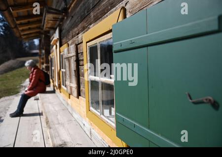 19 marzo 2022, Baviera, Großweil: Una donna gode il sole sulla panchina di una storica fattoria sui terreni del museo all'aperto Glentleiten. Dopo la polvere del Sahara, il sole primaverile si ripresenta nel cielo nuvoloso. Foto: Angelika Warmuth//dpa Foto Stock