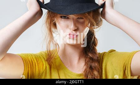 Perché entrare in forma quando siete nati per distinguersi. Primo piano ritratto studio di una bella donna giovane pouting indossando un cappello nero. Foto Stock
