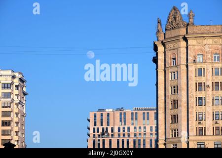 Luna piena rotonda su un cielo senza nuvole aggrovigliato in fili tra i tetti delle grandi case della città in serata Foto Stock