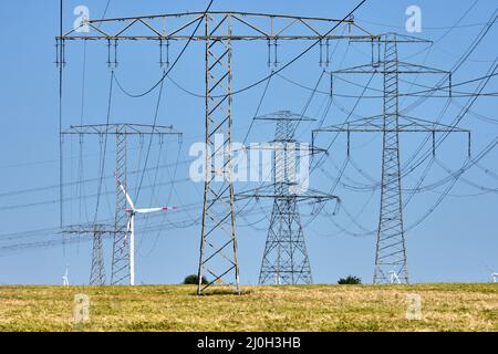 Piloni elettrici e linee elettriche con turbine eoliche sullo sfondo visto in Germania Foto Stock