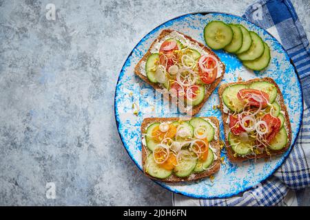 Piastra con toast con cucomber, pomodori e feta sbriciolata e germogli di rafano Foto Stock