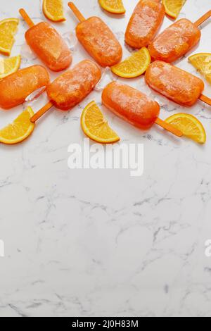 Pop sicle surgelate fatte in casa con arance fresche oragniche poste con cubetti di ghiaccio sul tavolo di marmo Foto Stock