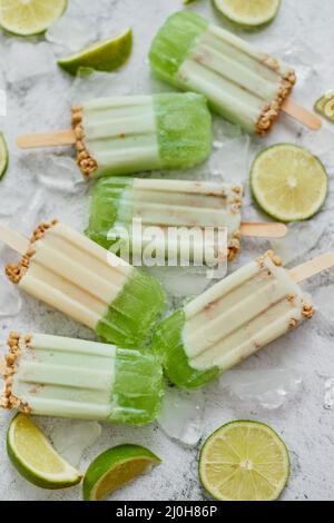 Lime e panna fatta in casa popsicles o gelati messi con cubetti di ghiaccio su sfondo di pietra grigia Foto Stock