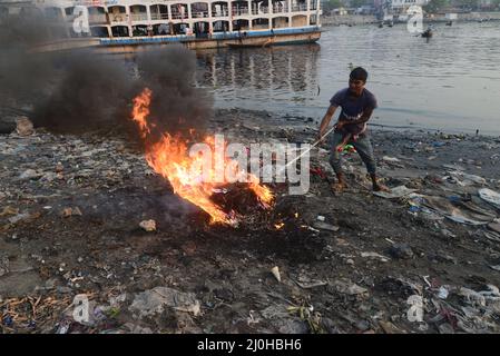 Dhaka, Bangladesh . 19th Mar 2022. La gente brucia i rifiuti crea fumo tossico sulla riva del fiume Buriganga a Dhaka, Bangladesh, il 19 marzo 2022. Dhaka continua ad essere classificata come una delle città più inquinate del mondo, con i detriti derivanti da costruzioni, emissioni di veicoli e forni in mattoni elencati come i principali fattori che contribuiscono all'inquinamento atmosferico della città. Credit: Mamunur Rashid/Alamy Live News Foto Stock