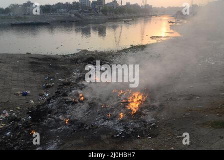 Dhaka, Bangladesh . 19th Mar 2022. La gente brucia i rifiuti crea fumo tossico sulla riva del fiume Buriganga a Dhaka, Bangladesh, il 19 marzo 2022. Dhaka continua ad essere classificata come una delle città più inquinate del mondo, con i detriti derivanti da costruzioni, emissioni di veicoli e forni in mattoni elencati come i principali fattori che contribuiscono all'inquinamento atmosferico della città. Credit: Mamunur Rashid/Alamy Live News Foto Stock