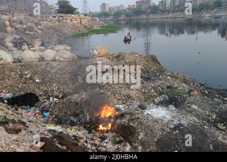 Dhaka, Bangladesh . 19th Mar 2022. La gente brucia i rifiuti crea fumo tossico sulla riva del fiume Buriganga a Dhaka, Bangladesh, il 19 marzo 2022. Dhaka continua ad essere classificata come una delle città più inquinate del mondo, con i detriti derivanti da costruzioni, emissioni di veicoli e forni in mattoni elencati come i principali fattori che contribuiscono all'inquinamento atmosferico della città. Credit: Mamunur Rashid/Alamy Live News Foto Stock