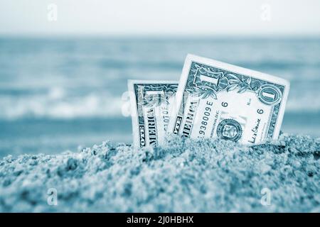 Due bollette da un dollaro mezzo sepolto in sabbia su sabbia sabbiosa spiaggia primo piano. Foto Stock