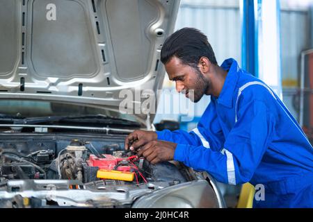 Test o controllo della batteria del motore dell'automobile da parte del meccanico dell'automobile usando il multimetro digitale al garage - concetto di tecnologia, servizi di manutenzione e blu Foto Stock