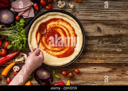 Pasta di pizza cruda e deliziosa con souce rosso sul tavolo di legno Foto Stock