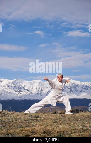 Wushu maestro in uno sport bianco uniforme di allenamento kungfu in natura sullo sfondo di montagne innevate. Foto Stock