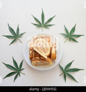 Rotolo dolce con olio di marijuana su piatto bianco. Cucina di cannabis. Disposizione dei deliziosi dessert, vista dall'alto da vicino. Foto Stock