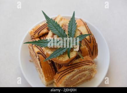 Rotolo dolce con olio di marijuana su piatto bianco. Cucina di cannabis. Disposizione dei deliziosi dessert, vista dall'alto da vicino. Foto Stock