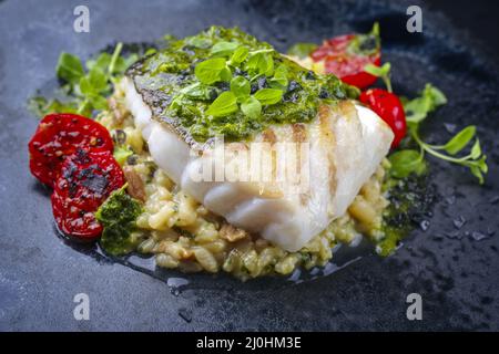 Filetto di pesce di merluzzo fritto in stile moderno con risotto di riso ai funghi e salsa all'origano servito da vicino su un Foto Stock