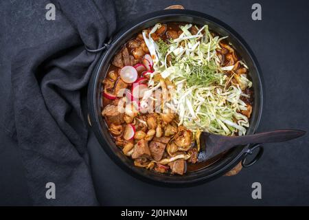 Tradizionale zuppa messicana di rojo di pozole a cottura lenta con carne di maiale e maiz hominy servito come vista dall'alto in un design moderno in ghisa Foto Stock