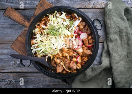 Tradizionale zuppa messicana di rojo di pozole a cottura lenta con carne di maiale e maiz hominy servito come vista dall'alto in un design moderno in ghisa Foto Stock