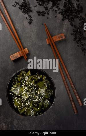 Insalata di alghe di wakame. Ciotola e bastoni di bambù. Servizio orientale. Vista dall'alto. Foto Stock