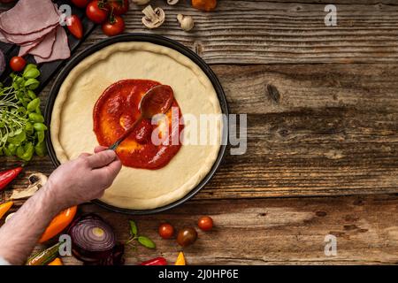 Pasta di pizza cruda e deliziosa con souce rosso sul tavolo di legno Foto Stock