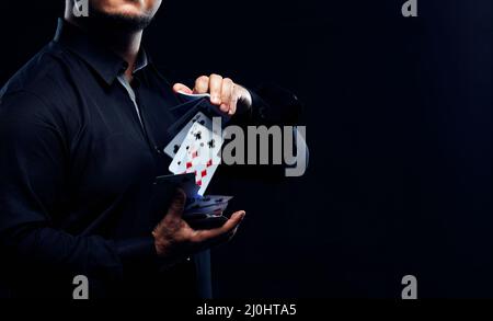 Il mago illusionista che mostra come eseguire il trucco della scheda. Primo piano di carte di mano e poker su sfondo nero. Foto Stock