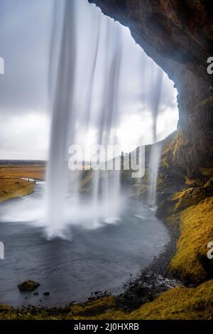 Cascata di Seljalandsfoss nell'Islanda meridionale. Visto da una grotta dietro. I fotografi non identificabili scattano dall'altra direzione. Toni autunnali. Foto Stock