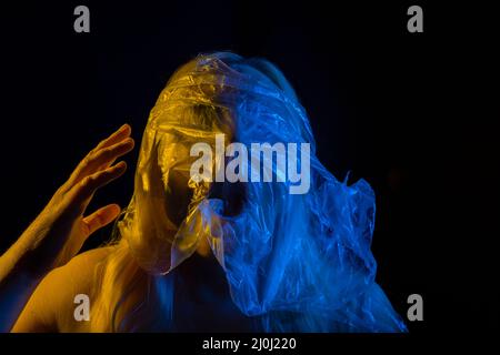 Donna con il viso coperto di borsa di nylon, urlando nella paura e nel dolore, illuminata con colori bandiera Ucraina, giallo e blu, sfondo nero Foto Stock