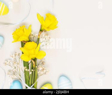 Composizione per le vacanze di Pasqua con bouquet di naffodoli gialli con nastro e uova di pasqua su sfondo bianco con spazio per la copia adatto per le congratulazioni Foto Stock