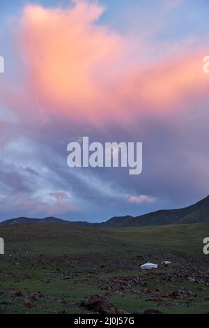 Paesaggio mongolo con steppa di montagna sotto le nuvole di cumuli in corso sul cielo del tramonto, yurts e mandria di capre Foto Stock