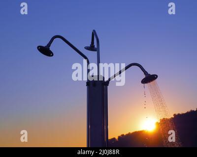 Tre docce sulla spiaggia con un ruscello da una delle lattine d'acqua sullo sfondo del sole che tramonta Foto Stock